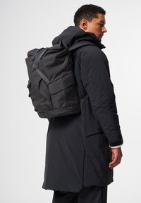 Schwarzer Rucksack aus robustem Material, mit verstellbaren Tragegurten, einem Rollverschluss und mehreren Außentaschen für Stauraum.