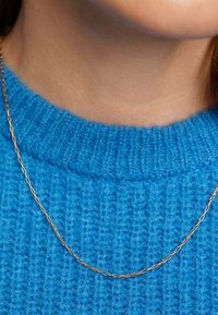 Collar de cadena de oro sobre un suéter de punto azul, con un diseño de eslabones alargados y una textura suave, descansando en el cuello.