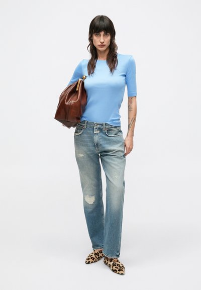 Top azzurro a maniche corte, jeans azzurri strappati, borsa in pelle marrone e mocassini con stampa animalier. Outfit casual con texture variegate.