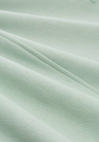 Tessuto verde chiaro con una superficie texture, caratterizzato da pieghe e grinze, che evidenziano la sua qualità morbida e traspirante.