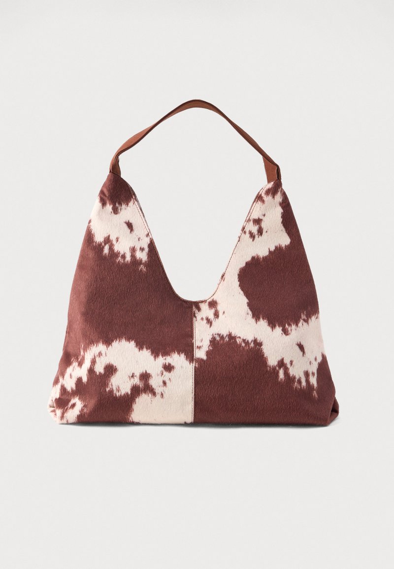 Saco hobo com padrão de pelo de vaca castanho e branco, com uma única alça de couro e uma estrutura suave e descontraída sobre um fundo simples.