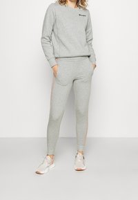 Sudadera gris y joggers a juego hechos de una tela suave. La sudadera tiene un pequeño logo, mientras que los joggers cuentan con franjas laterales rosas y bolsillos.