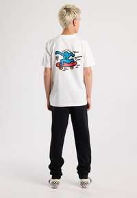 White cotton t-shirt featuring a colorful skateboard graphic on the back. Paired with black sweatpants and checkerboard slip-on shoes.