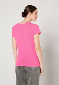 Camiseta de manga corta y cuello redondo en color rosa brillante, hecha de tejido ligero con un acabado texturizado. Espalda lisa sin detalles prominentes.