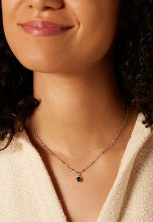 Silberne Kettenhalskette mit einem kleinen grünen Edelstein-Anhänger. Die Halskette ist zart und sitzt direkt über dem Schlüsselbein.