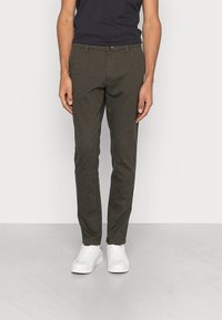 Slim-fit, donkergroene broek van gestructureerde stof. Voorzien van een knoopsluiting, twee voorkruiszakken en subtiele patroon details. Gekocht met witte sneakers.