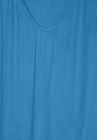 Helles blaues Stoffoberteil mit einem runden Ausschnitt, das eine weiche, strukturierte Oberfläche und subtile Falten für einen entspannten Look aufweist.