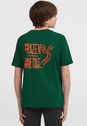 Grön bomullströja med korta ärmar. Baksidan pryds av en livlig orange grafisk text som säger "FROZEN WAVE CULT" tillsammans med en illustration.