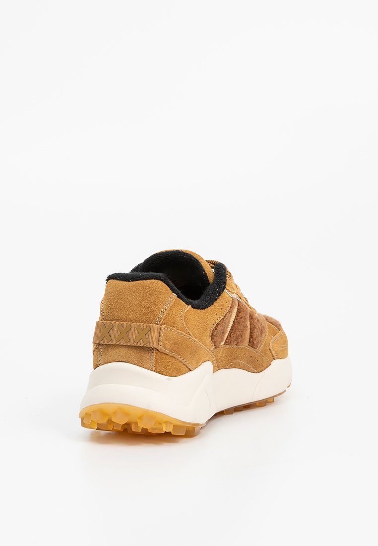 Tan suède sneakers met een textuur bovenkant, zwarte accenten en een dikke witte buitenzool. Kenmerken zijn zichtbare stiksels en een gebloemde hielaccent.