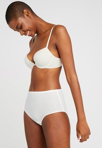 White high-waisted briefs paired with a light beige bra. Features smooth texture, adjustable straps, and a minimalist design.