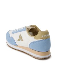 Sneaker bianco e azzurro chiaro con materiale in suede e pelle, punta rotonda, chiusura con lacci, logo dorato e dettaglio beige sul tallone.