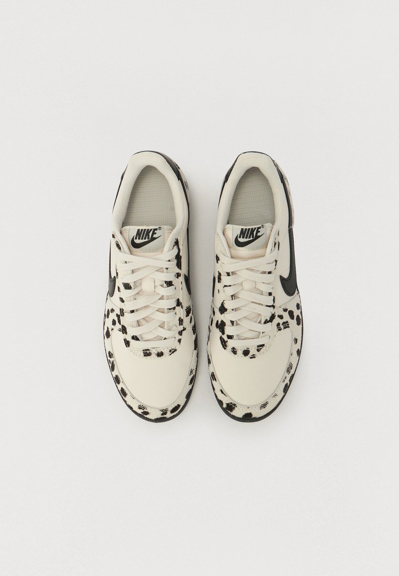Baskets Nike blanches avec des accents en imprimé léopard noir, présentant une tige texturée, des fermetures à lacets et un logo swoosh noir sur les côtés.