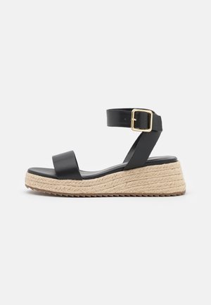 Zwarte leren espadrille sandaal met brede voorkeursband, enkelband die wordt vastgezet met een gouden gesp, en een getextureerde jute-wikkelzool.