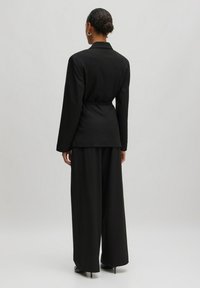 Black tailored blazer with long sleeves and a cinched waist, paired with wide-leg trousers. Smooth fabric, minimalist design, and sleek silhouette.