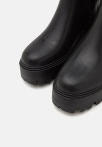 Black leather ankle boots with a rounded toe, chunky treaded sole, and visible stitching detail along the edge. Zipper closure on one side.