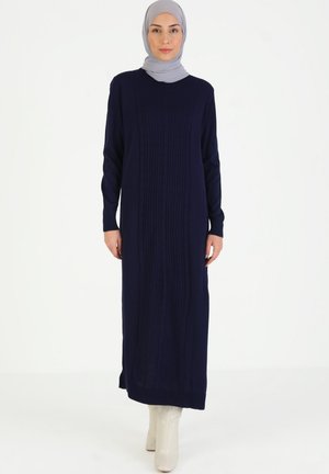Navy blue knitted dress with cable texture and long sleeves, featuring a round neckline and side slits, paired with a light gray hijab.