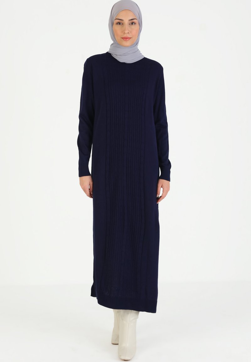 Abito lavorato a maglia blu navy con trama a treccia e maniche lunghe, caratterizzato da un girocollo e fessure laterali, abbinato a un hijab grigio chiaro.