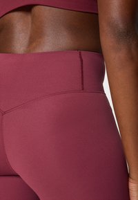 Bordeauxrote, hoch taillierte Leggings aus dehnbarem Stoff, mit flachen Nähten und einer glatten Textur für Komfort beim Training.