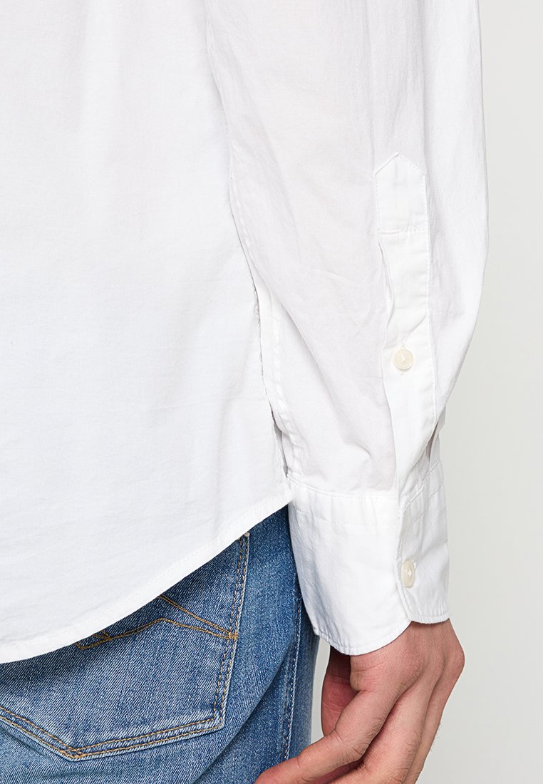 Weiße Langarmbluse aus Baumwolle mit geknöpften Manschetten und abgerundetem Saum, kombiniert mit blauen Jeans.