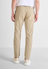 Pantalones de algodón beige con un diseño de pierna recta, dos bolsillos traseros y un dobladillo limpio, combinados con zapatillas de colores claros.