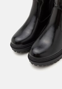 Sorte skinn ankle boots med blank overflate, rund tå, tykk svart gummisåle og lav profil. Har ingen synlige deler.