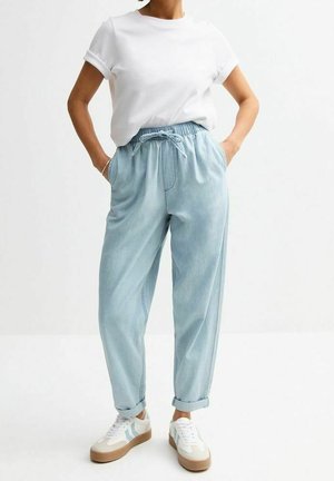 Vaaleansiniset, löysät farkut, joissa on joustava vyötärö ja nyöri, yhdistetty valkoiseen käänteet hihassa olevaan t-paitaan ja valkoisiin lenkkareihin.