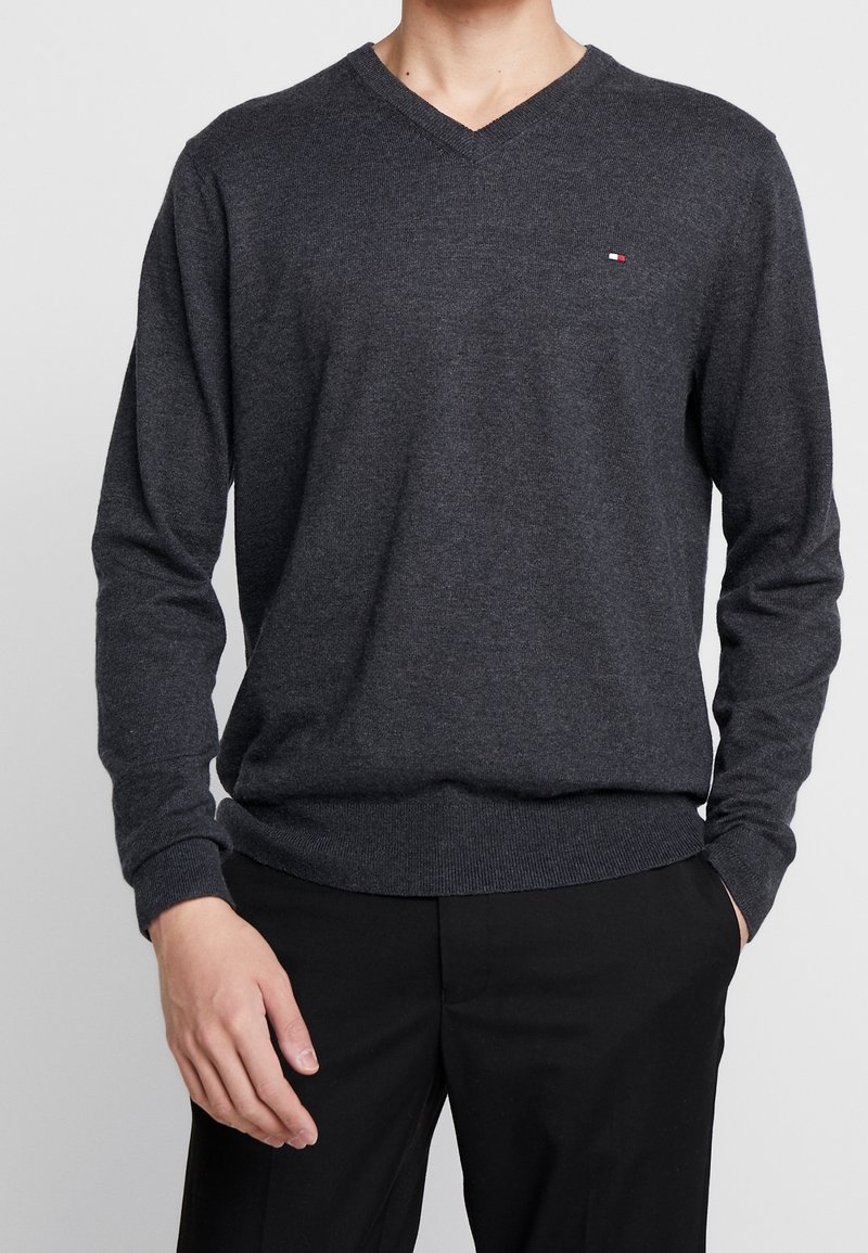 Ciemnoszary sweter typu v-neck z długimi rękawami, prążkowanymi mankietami i dołem. Mały akcent loga w czerwonym i białym kolorze na lewej piersi.