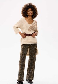 Beige gebreide trui met een V-hals en een lichte dierenprint, gecombineerd met high-waisted leopardprint broeken en een bruine riem. Zwarte laarzen.