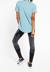 Lichtblauw T-shirt met korte mouwen, zwarte legging met geometrische patronen, en grijze sportschoenen met veters.