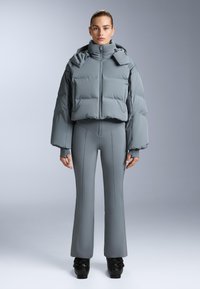 Padded grå pufferjacka med hög krage och översized ärmar, ihop med figurnära grå byxor med sömmar, som bärs med svarta skor.