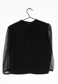 Schwarze Bluse mit solidem Körper und transparenten, gepunkteten Puffärmeln. Verfügt über einen Schlüsselaugenverschluss auf der Rückseite mit einer Knopfverschluss. Weiche Textur.