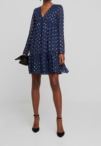 Marineblauwe jurk van lichte stof, met lange mouwen, een diepe V-hals, een gelaagde rok en zilveren bladpatronen.