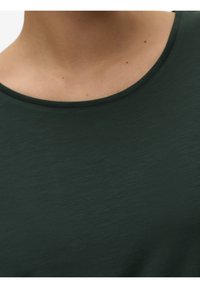 Ciemnozielona, krótko rękawowa koszulka z okrągłym dekoltem. Materiał ma miękką, delikatnie teksturowaną powierzchnię, z minimalnym cieniowaniem.