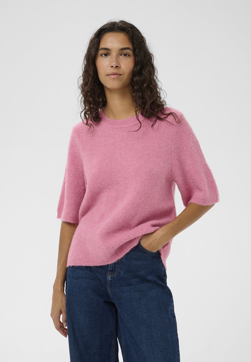 Rosa Kurzarm-Pullover aus weichem, flauschigem Material mit rundem Ausschnitt. Kombiniert mit dunkelblauen Jeans mit weitem Bein und lässiger Passform.