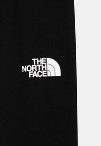 Czarna tkanina z białym logo The North Face, składającym się z stylizowanego kształtu półkuli i tekstu, po lewej stronie. Gładka tekstura.