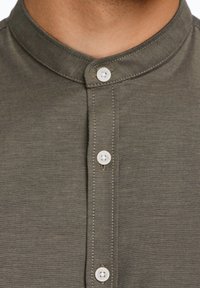 Donkergroene blouse met kraag en een knoopsluiting, voorzien van witte knopen en een gestructureerde stofafwerking.