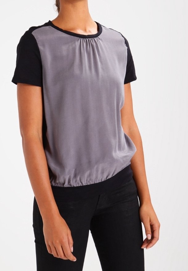 Grå satinblus med svarta korta ärmar, skrynklig hals och elastisk fåll. Buren med svarta byxor, som visar en avslappnad passform.