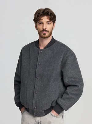 Giacca bomber in lana grigia con colletto a coste, caratterizzata da bottoni a pressione e polsini elasticizzati. Tessuto liscio, vestibilità ampia e design minimalista.