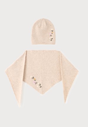 Bonnet en tricot beige et écharpe triangulaire assortie avec petits motifs floraux brodés en jaune, blanc et rose sur fond uni.