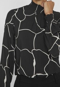 Černá blůza s dlouhým rukávem a bílým abstraktním vzorem, s nabíraným výstřihem a manžetami, vyrobena z jemné tkaniny s volným designem.
