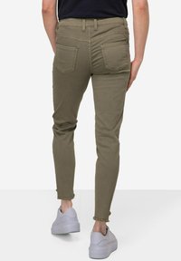Khaki skinny džíny s středně vysokým pasem, obsahující dvě zadní kapsy a třepené lemy, doplněné bílými teniskami.