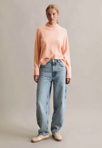 Helles rosa geripptes Sweatshirt, kombiniert mit lässigen blauen Jeans. Das Outfit hat eine lockere Passform, mit einem hohen Kragen und strukturiertem Stoff.