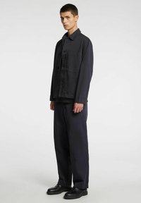 Tumesinine nööbitav jakk rinnataskuga, millele on lisatud sobivad laiade säärtega püksid. Sile kangas ja lõdvestunud lõige, mida täiustavad mustad kingad.