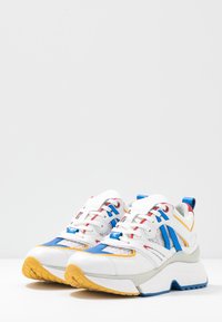 Vita chunkiga sneakers med blå, röda och gula accenter, texturerade sidopaneler, vita snören och tjocka sulor med gul och blå mönstring.