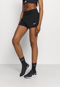 Svarta Nike-shorts med hög midja, med perforerad textur och sidofickor. Matchas med svarta Nike-strumpor och skor.