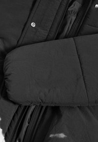 Giubbotto piumino nero con maniche trapuntate, caratterizzato da una texture liscia, bottoni metallici e chiusura frontale con zip.