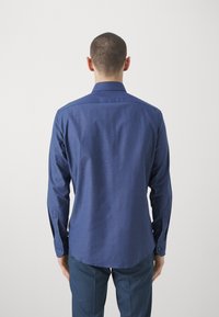 Pánská košile s dlouhým rukávem v tmavě modré barvě, vyrobená z texturované látky, s ostrým límcem a manžetami na knoflíky, pohled zezadu.
