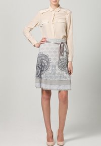 Blusa beige con bolsillos abotonados combinada con una falda gris con estampado que presenta un lazo y un borde de encaje en el dobladillo.