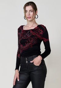 Čierny top s dlhým rukávom a červeným paisley vzorom, štvorcový výstrih a nariasenie na pleciach; skombinovaný s čiernymi nohavicami s vysokým pásom a gombíkmi.