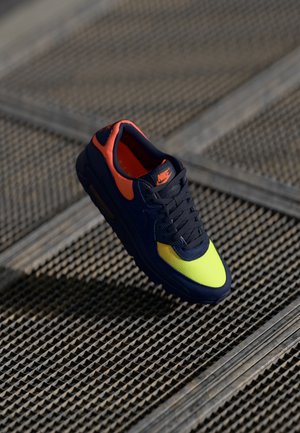 Nike sneaker featuring a dark navy upper, bright yellow toe, and orange accents; textile material and breathable design.